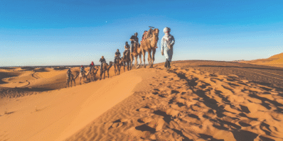 Camel tour in the Merzouga desert, Morocco, with travelers riding through golden sand dunes at sunset.